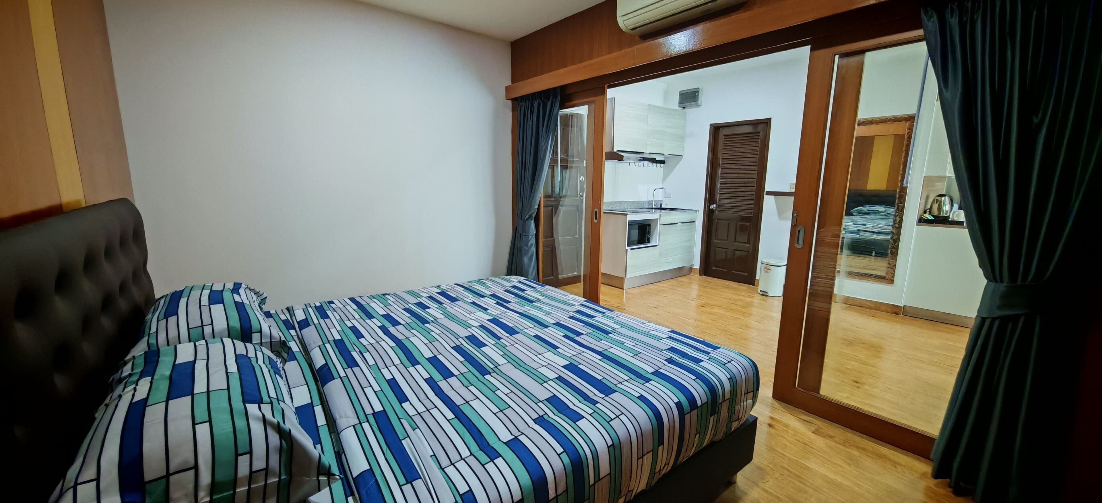 A bedroom with a bed, a wardrobe, and a sliding door leading to a kitchen area.