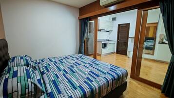 A bedroom with a bed, a wardrobe, and a sliding door leading to a kitchen area.