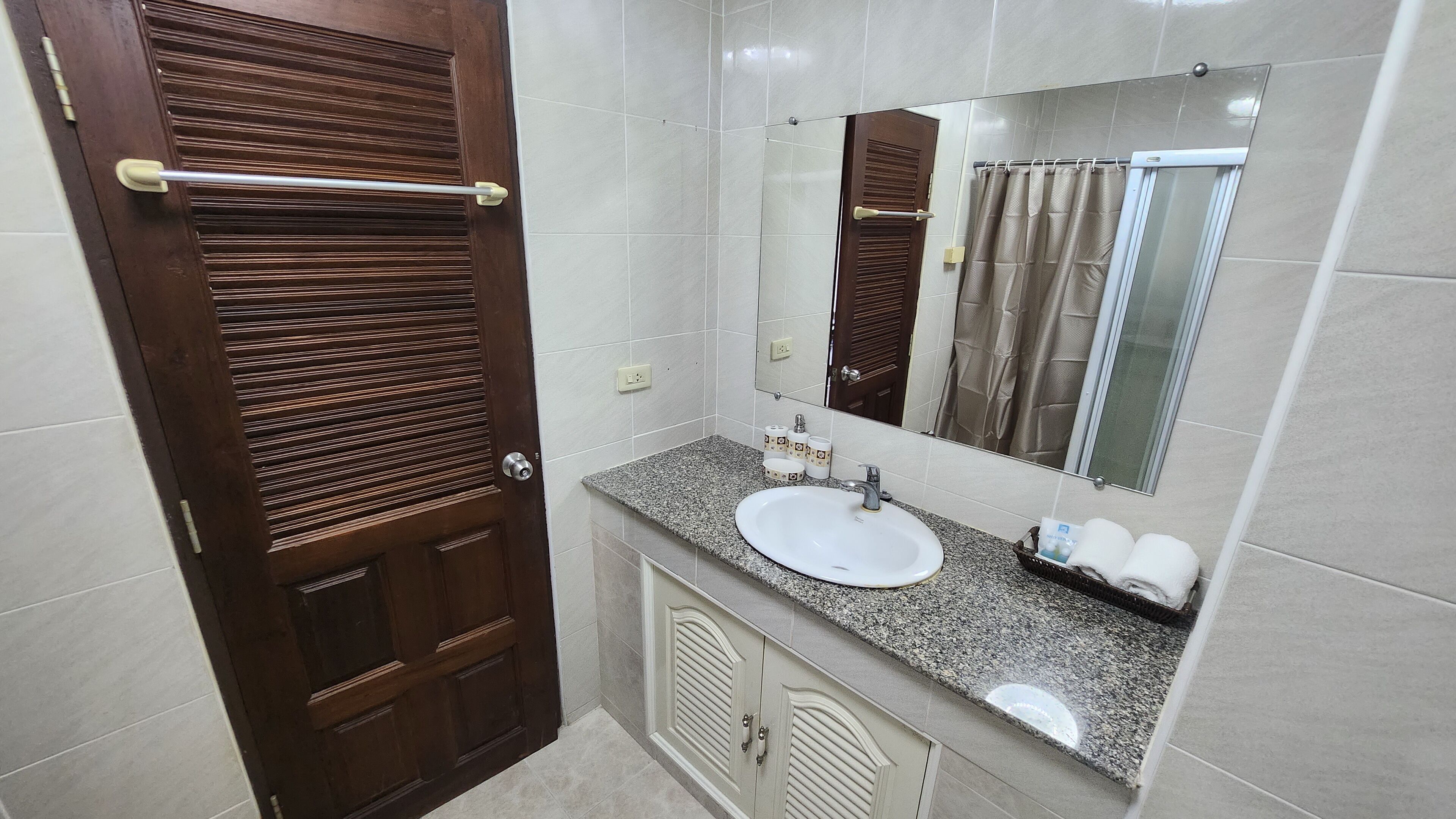A bathroom with a wooden door, a sink, a mirror, and a towel rack.