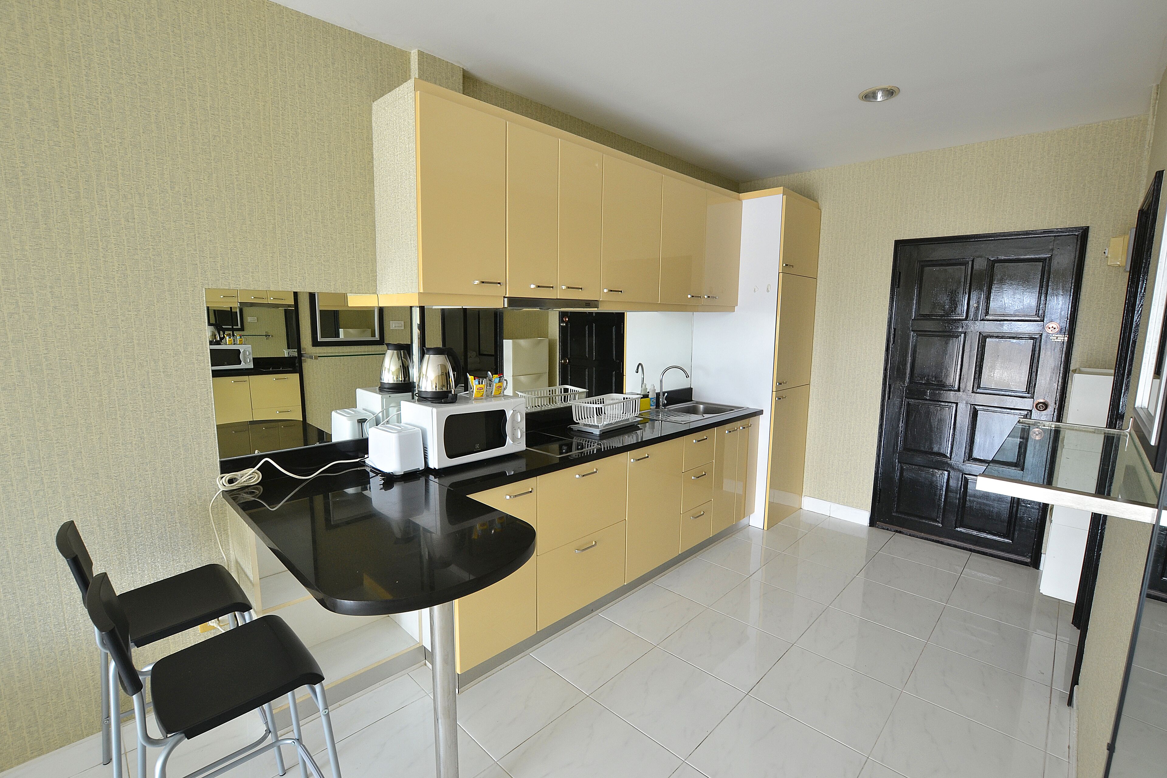 A modern kitchen with a black countertop, yellow cabinets, and a black door.
