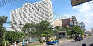 A multi-story building with a grid-like facade, surrounded by greenery and a busy street with vehicles. - Condo Express View Talay 6 (Pattaya)