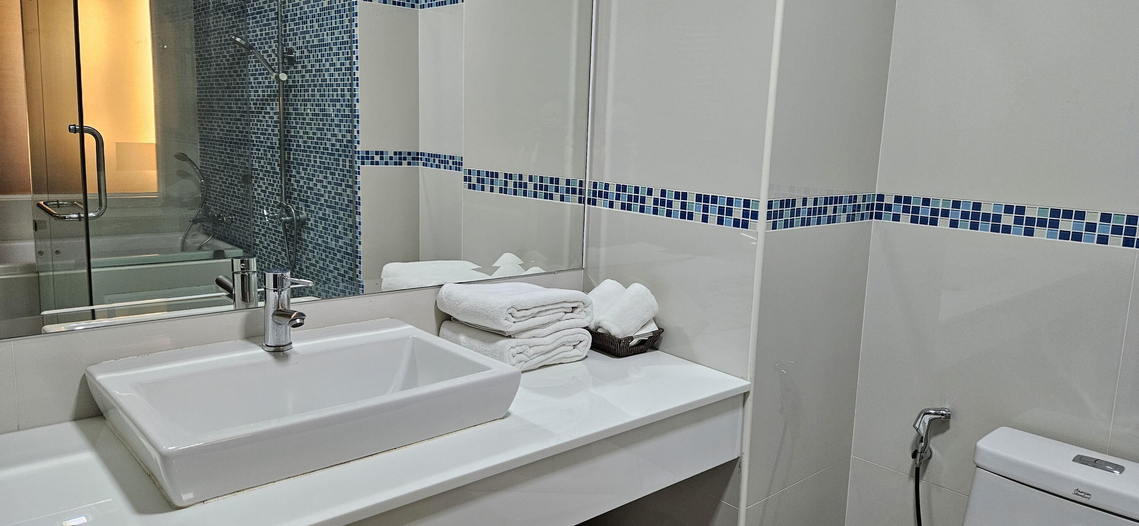 A modern bathroom with a large white sink, a glass shower enclosure, and a tiled wall with blue accents.