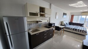 Una cocina moderna con refrigerador, pileta y alacenas, un comedor con mesa y sillas, y un dormitorio con cama y ventana.