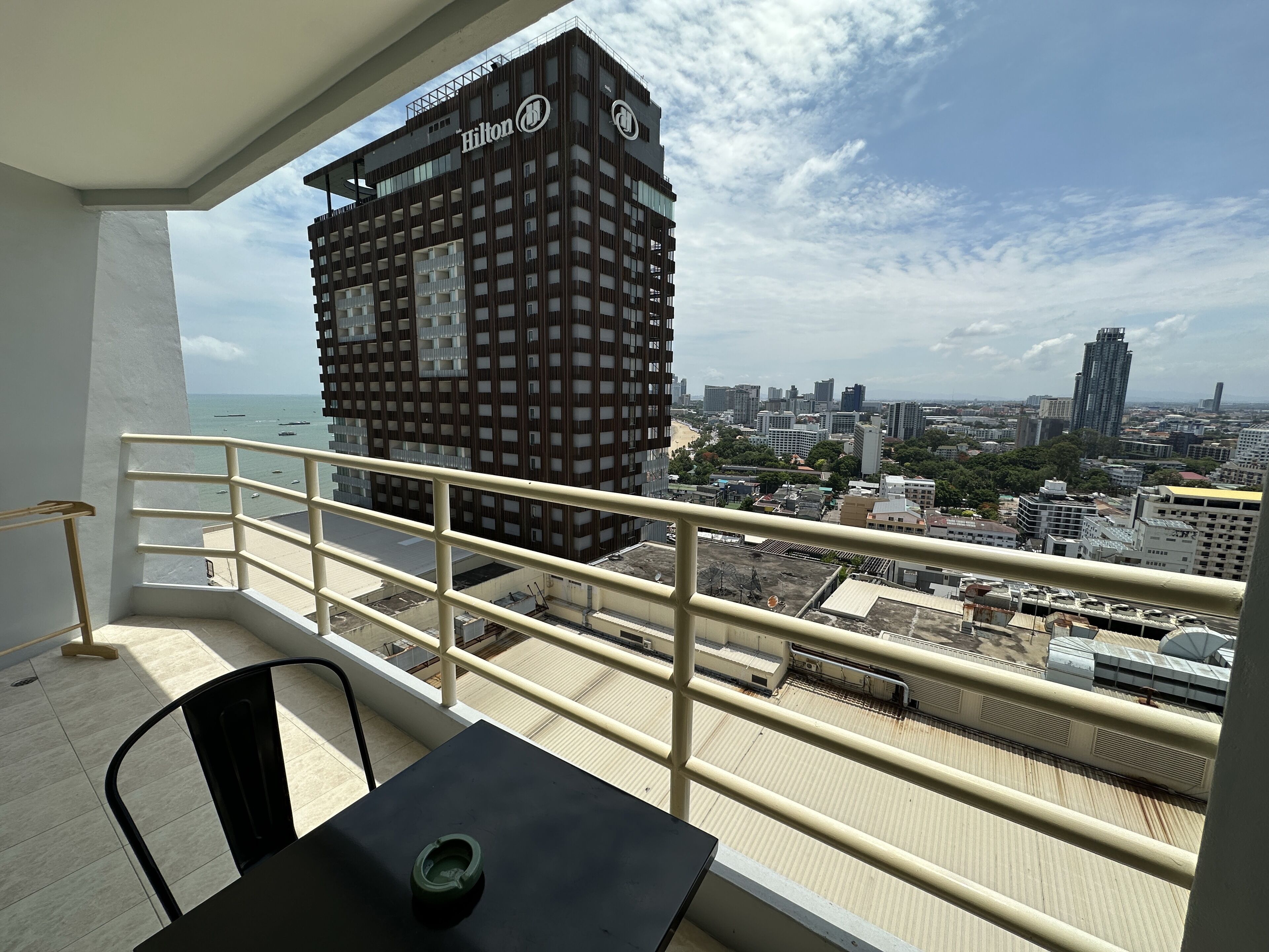 A balcony with a view of a Hilton hotel, cityscape, and beach.