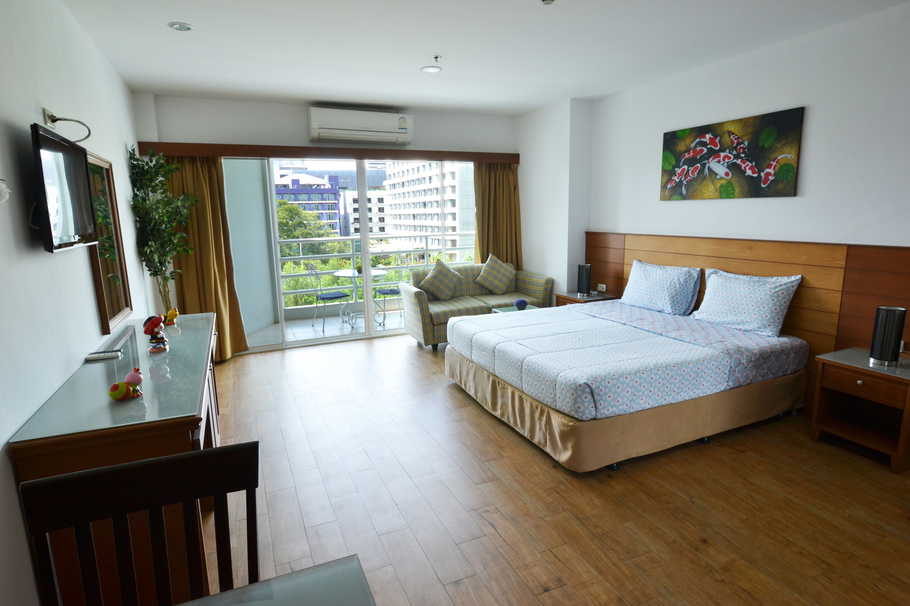 Habitación de hotel con cama, escritorio, silla, televisor, un cuadro y balcón con vistas a edificios.