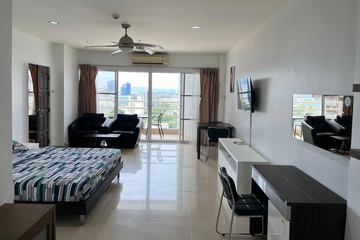 Ein modernes Hotelzimmer mit Bett, Schreibtisch, Sessel, Sofa, Deckenventilator und Fernseher.