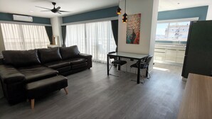 Uma sala de estar moderna com um sofá de couro preto, uma mesa de jantar de vidro com duas cadeiras e um ventilador de teto.