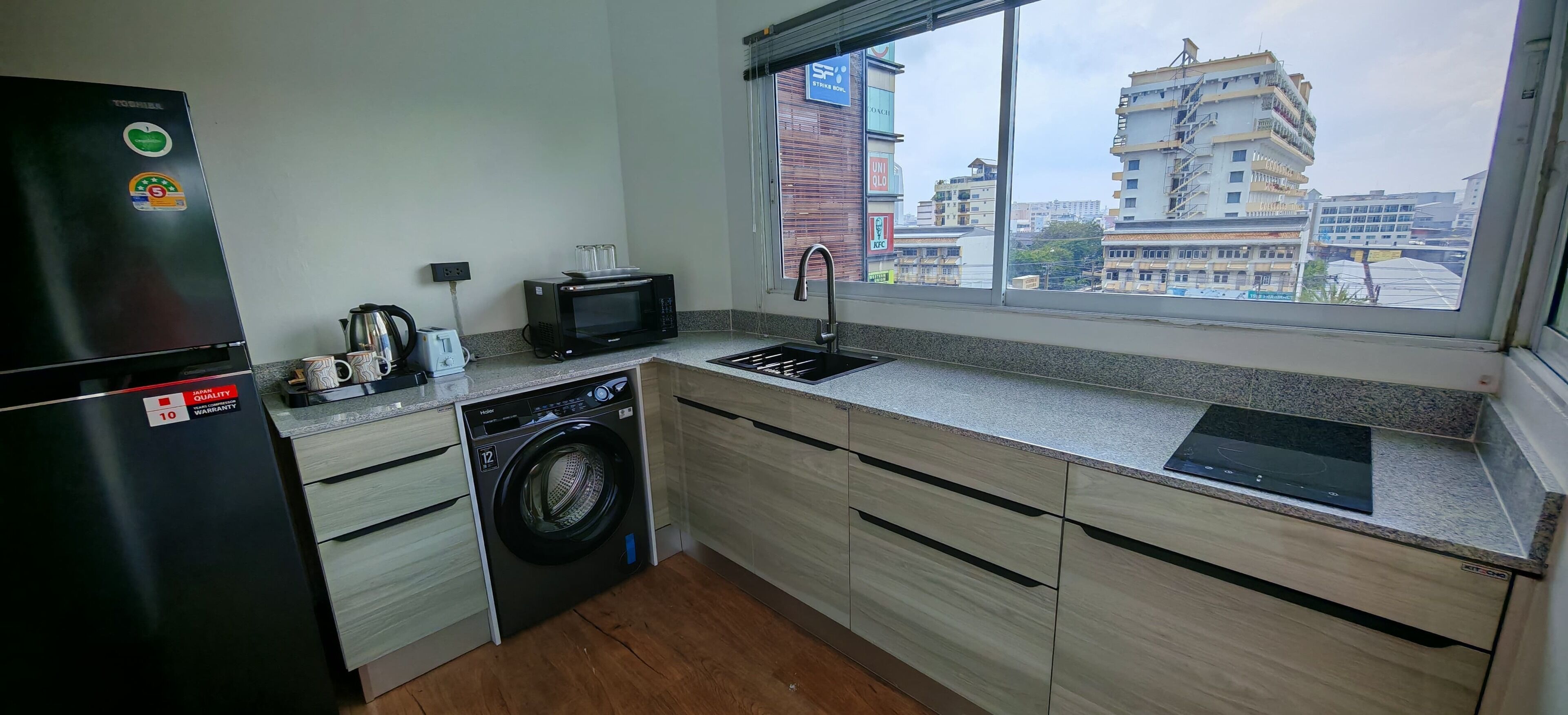 A compact kitchen with a washing machine, a microwave, and a toaster. It features a window with a city view.