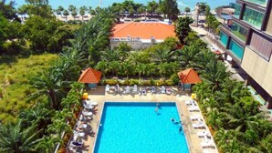 Um hotel com piscina rodeada por palmeiras, área de praia e vista para o mar com barcos.