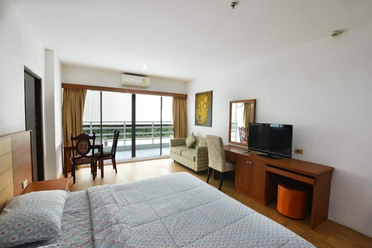 Ein Hotelzimmer mit Bett, Schreibtisch mit Fernseher, Sessel, Sofa und Balkon mit Vorhängen.