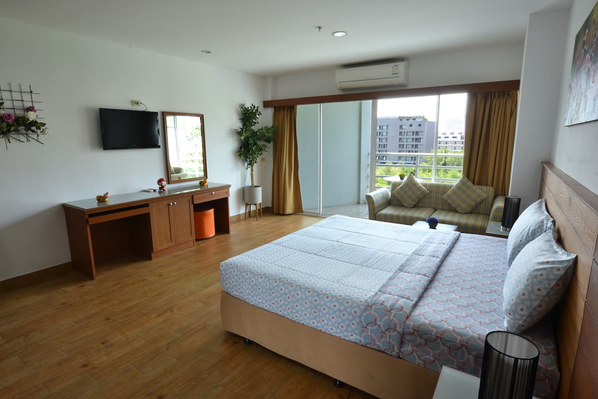 Ein Schlafzimmer mit einem großen Bett, einem Schreibtisch, einem Stuhl, einem Fernseher und einem Balkon mit Blick auf Gebäude.