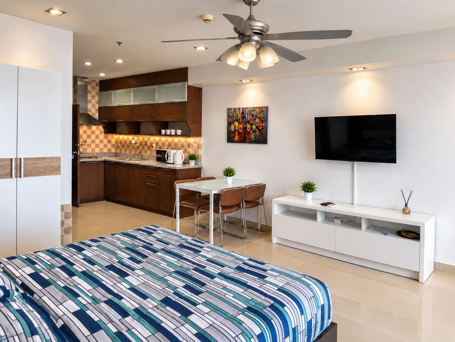 A modern bedroom with a large bed, a dining area, a kitchenette, and a TV.