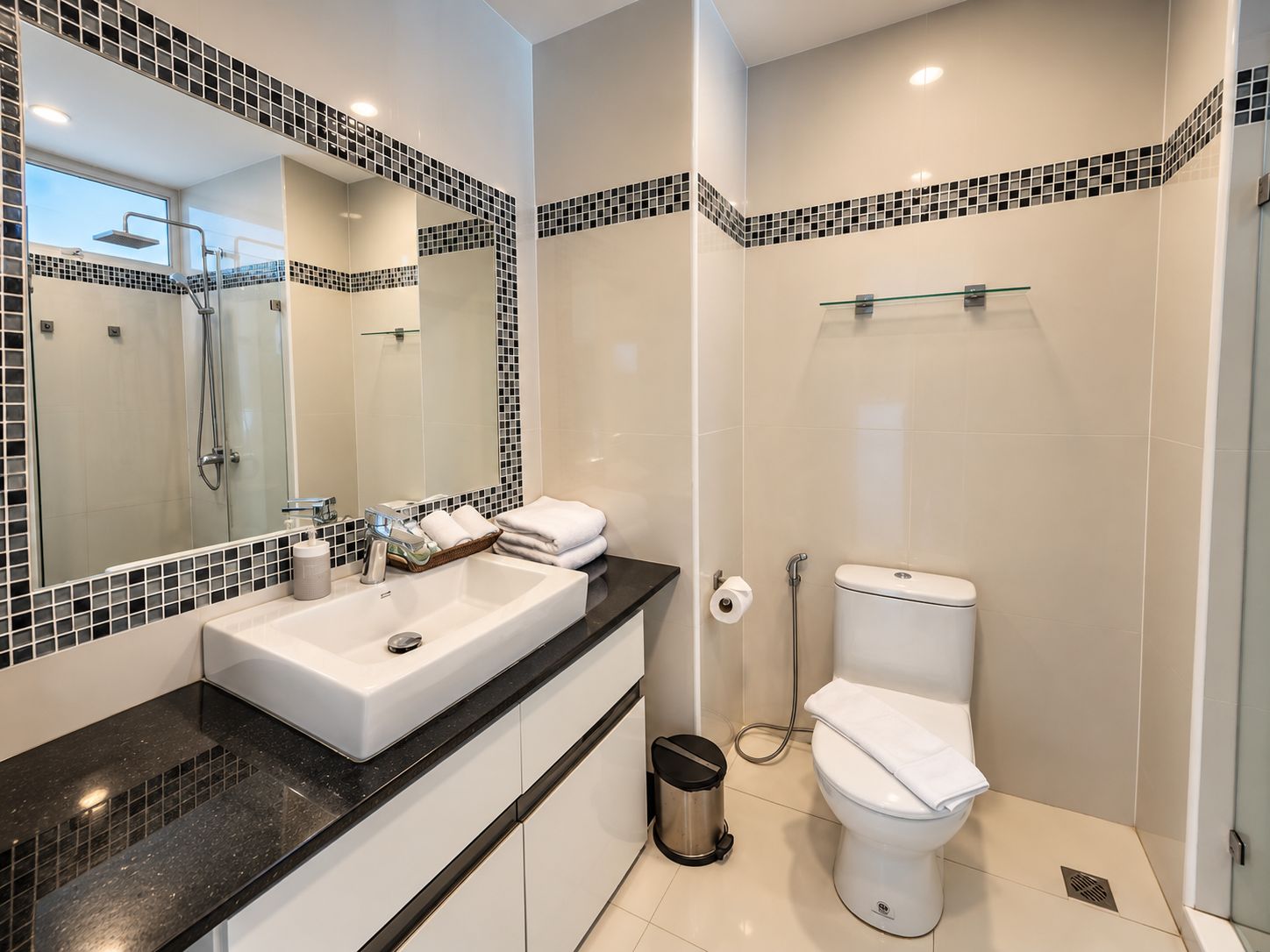 A bathroom with a white sink, mirror, and toilet, a glass shower enclosure, and a tiled backsplash.