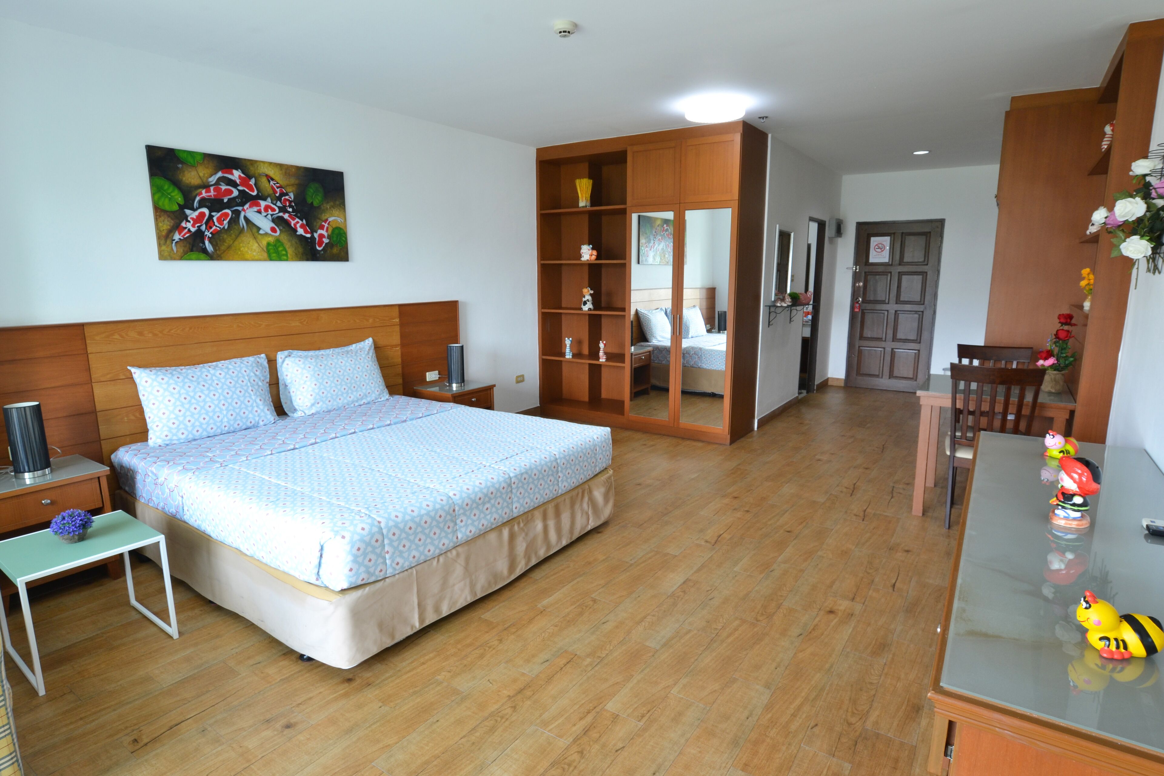 Quarto com cama de madeira, mesa de cabeceira, pequena mesa, espelho e cómoda.