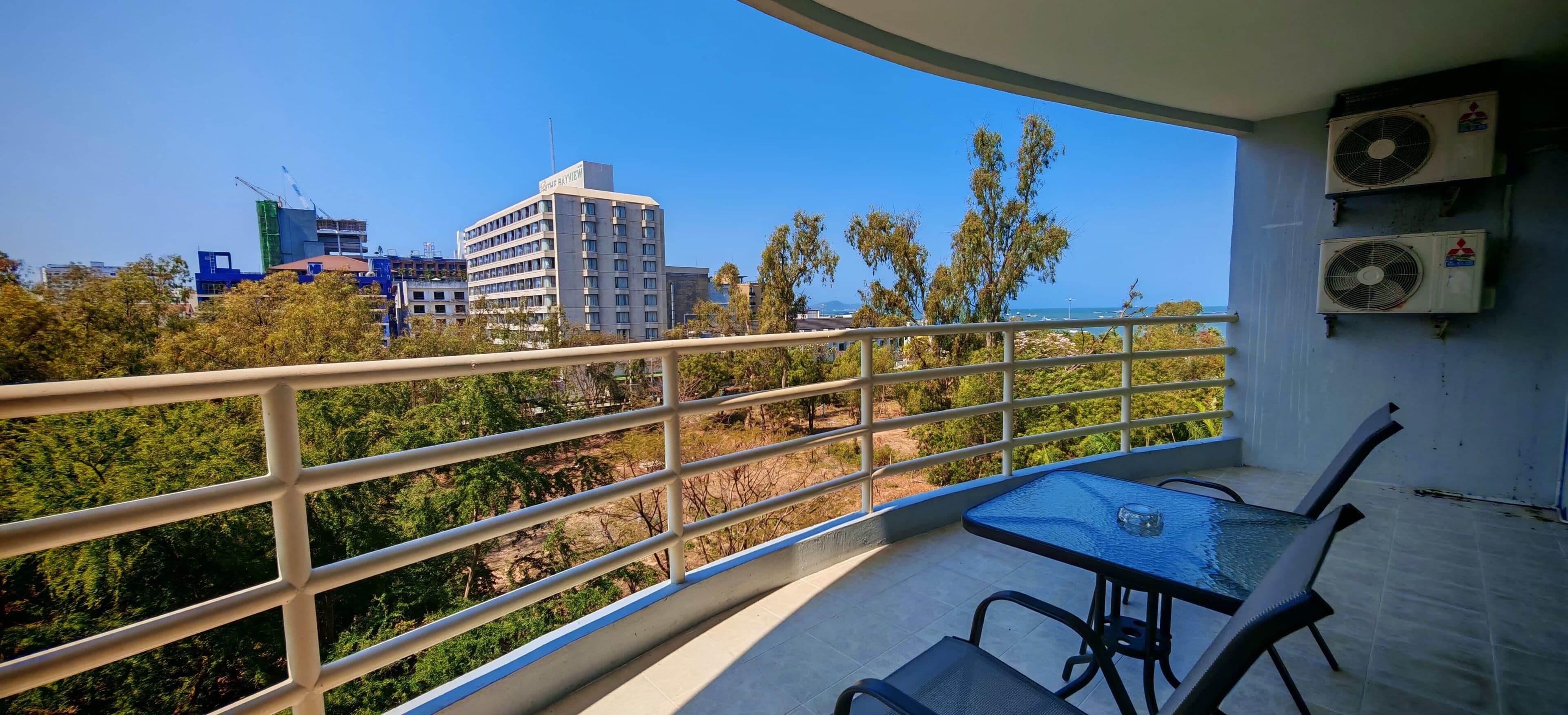A balcony with a table and chairs, overlooking a cityscape with buildings and trees.