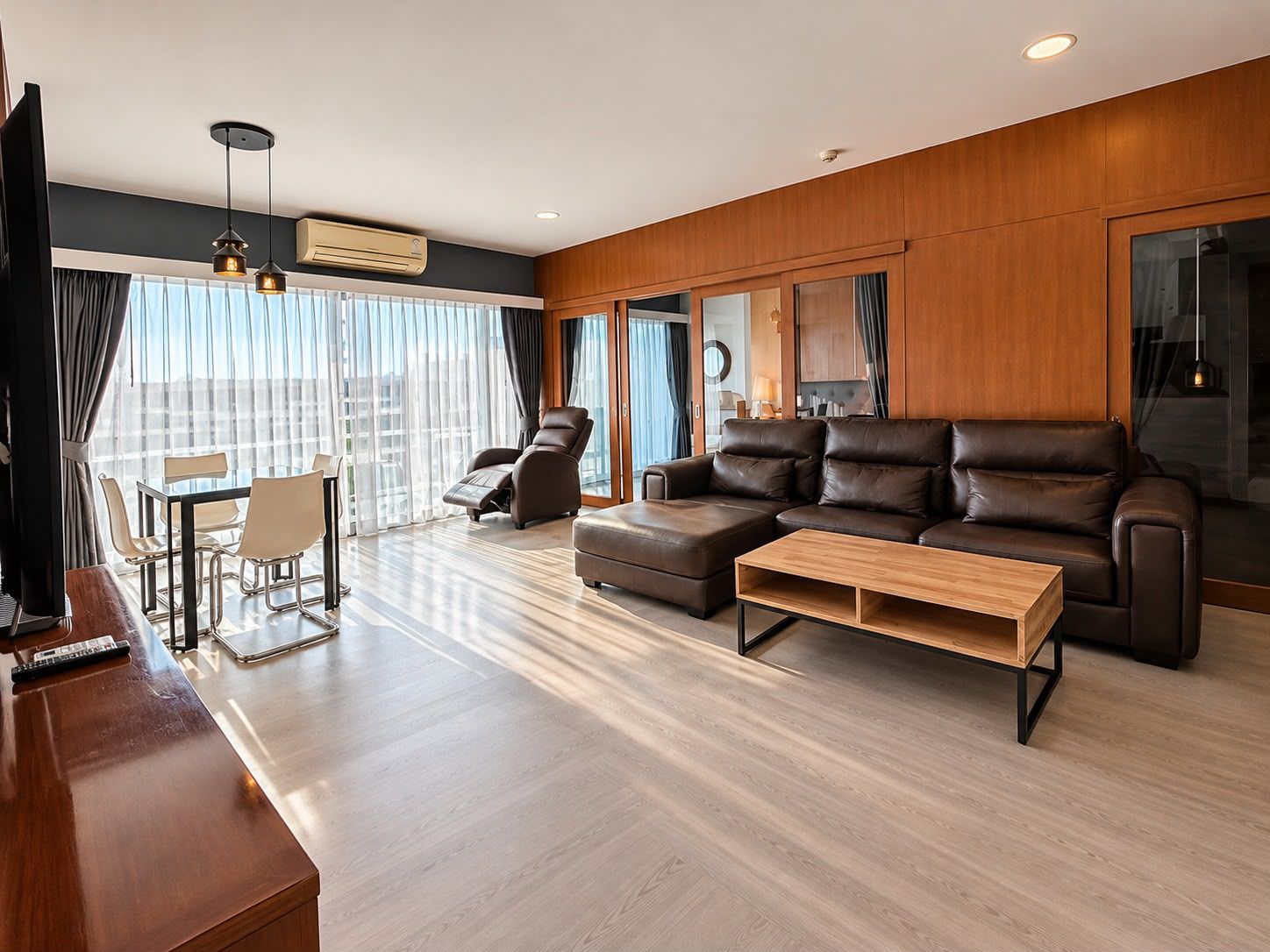 A modern living room with a sofa, armchair, and a coffee table. There is a dining area with a table and chairs.