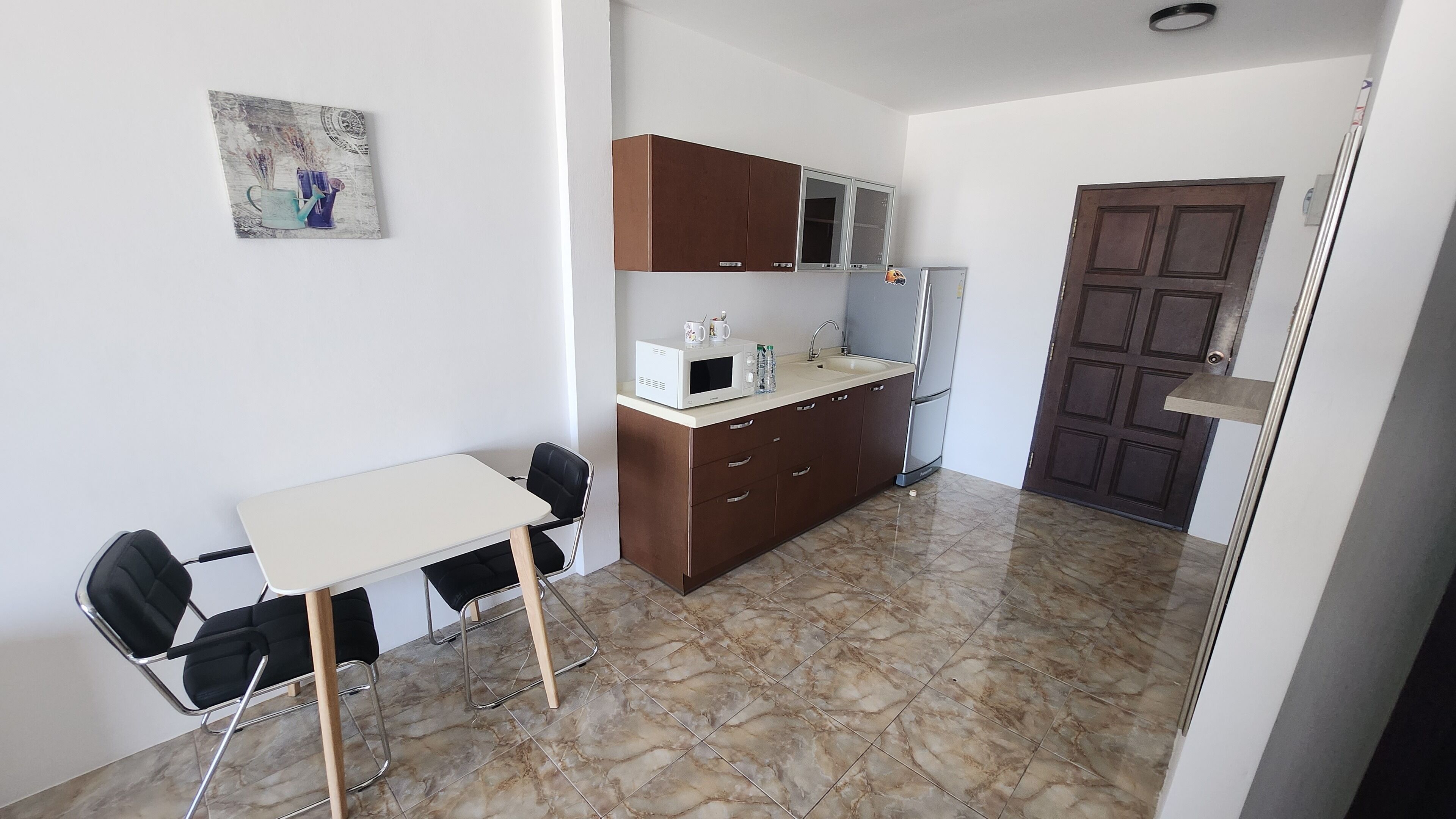 A small kitchenette with a microwave, refrigerator, and sink. There is a table with two chairs and a small cabinet above it.