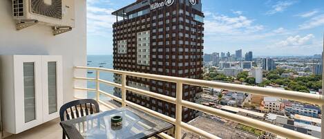 A balcony with a glass table and chairs, overlooking a cityscape with a prominent Hilton building.