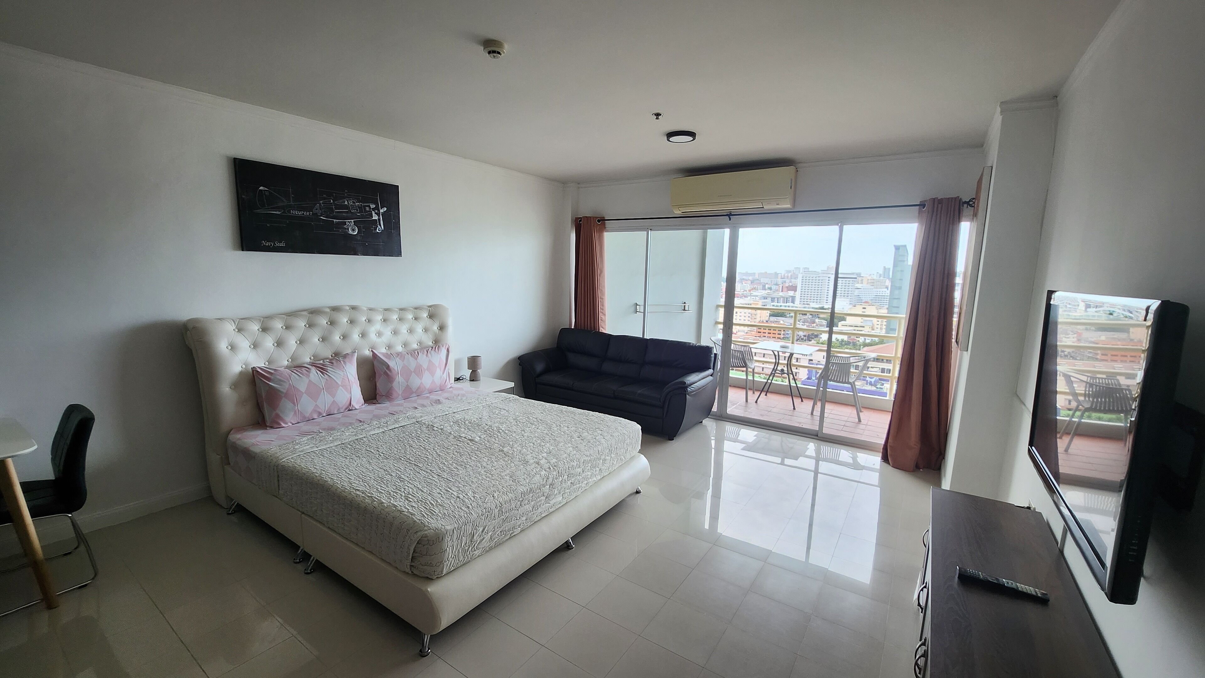 A modern bedroom with a large bed, a black sofa, a TV, and a balcony with a city view.