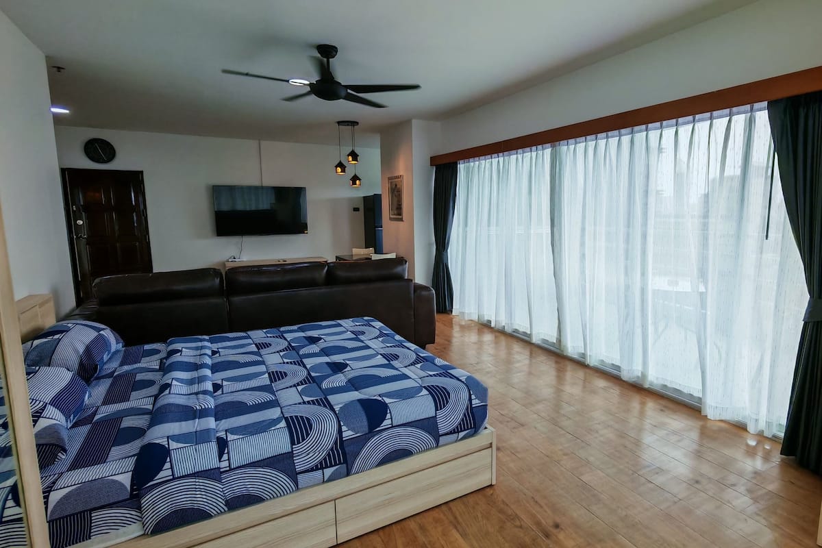 Ein Schlafzimmer mit Bett, Deckenventilator, Fernseher und einem großen Fenster mit Vorhängen.