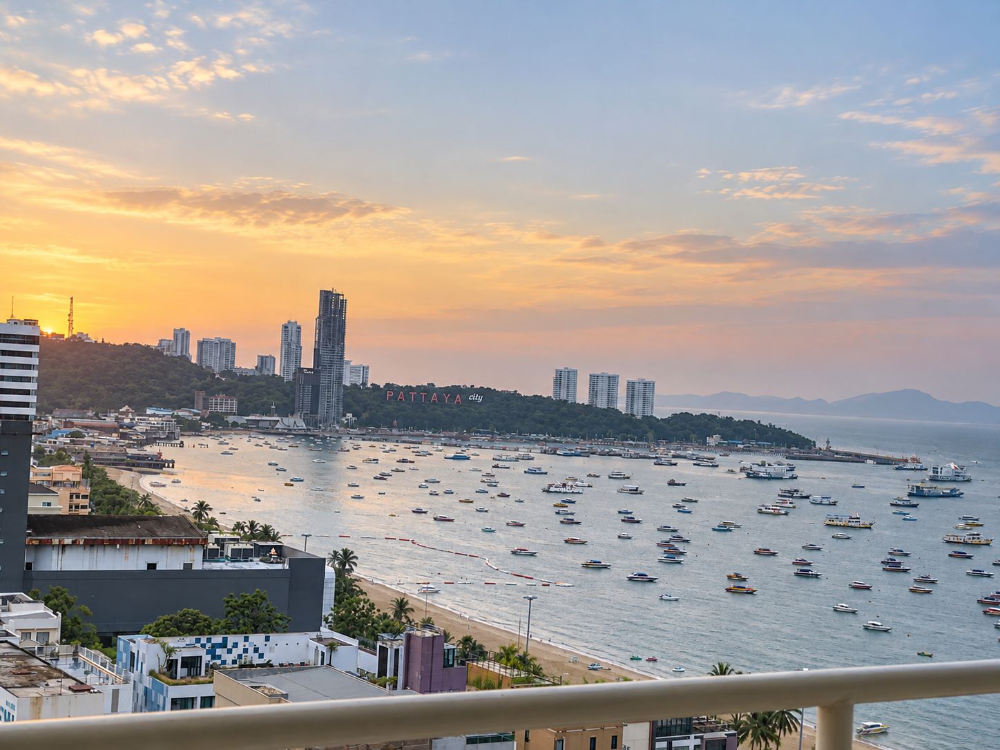 Paesaggio costiero con vista sul mare, numerose imbarcazioni e il profilo della città al tramonto.
