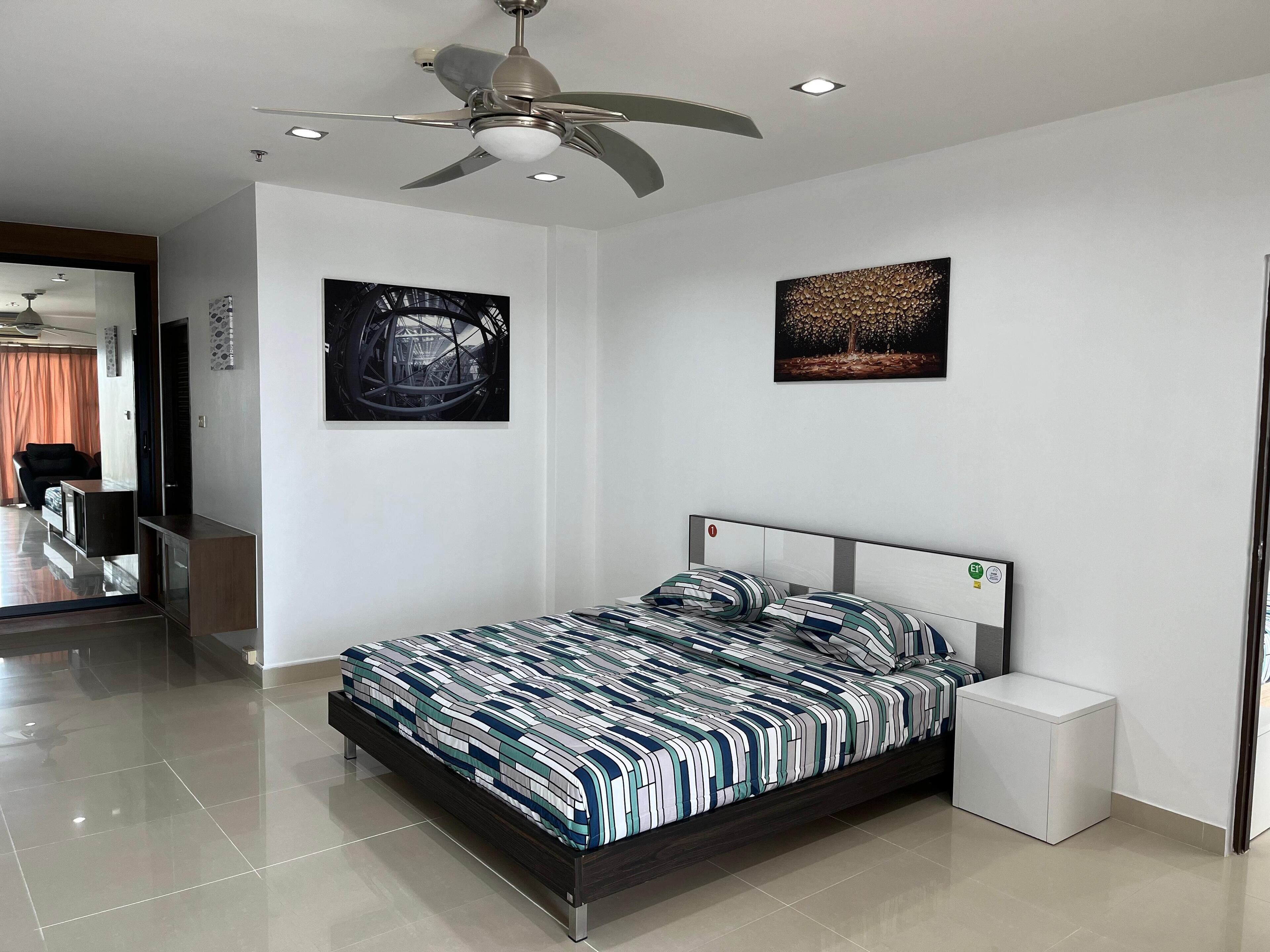 Un dormitorio moderno con una cama grande, un ventilador de techo y dos obras de arte en la pared.