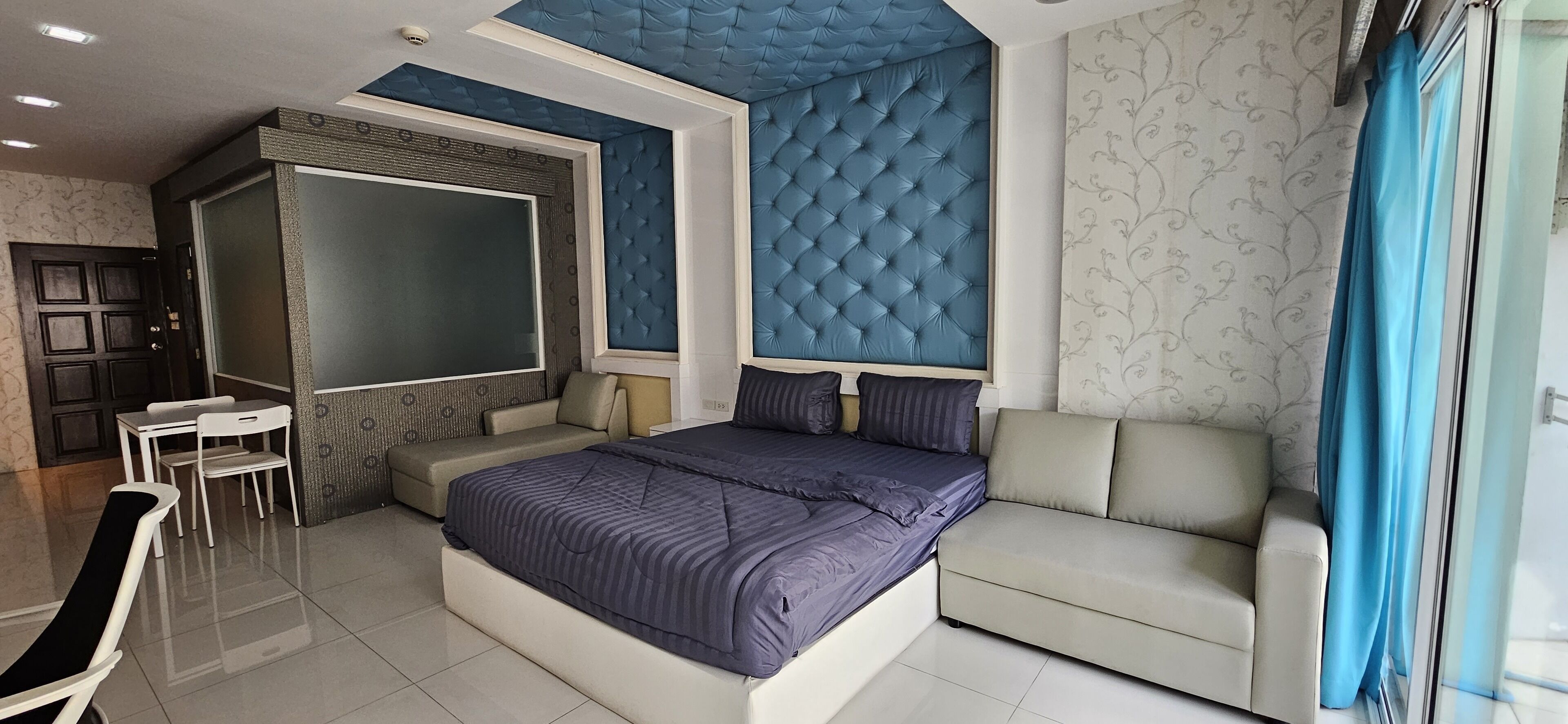 A modern bedroom with a large bed, a sofa, a desk, and a chair.