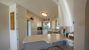 Una cocina moderna con armarios blancos, una isla curvada y dos taburetes de mimbre.