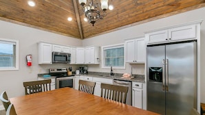A kitchen with white cabinets, a wooden ceiling, a stainless steel refrigerator, and a dining table with chairs.