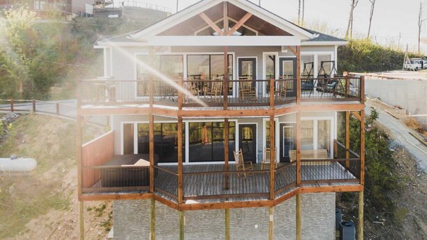 A multi-level wooden structure with balconies, large windows, and a view of the surrounding landscape.