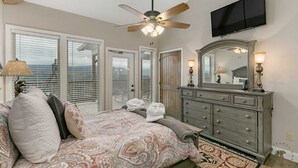 A bedroom with a bed, a ceiling fan, a dresser, a mirror, and a television.