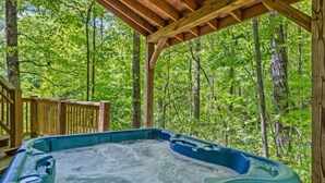 A hot tub in a forested area with a wooden deck and a pergola overhead.