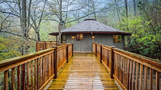 A wooden staircase leading to a cabin with a peaked roof, surrounded by trees.