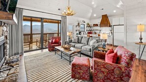 A spacious living area with a fireplace, a large window overlooking a scenic view, a cozy seating area, and a kitchen in the background. - Haven| DogFriendly | BEST View | Hot Tub | Luxury (Gatlinburg)