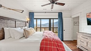A bedroom with a bed, a ceiling fan, a dresser, and a large window with curtains. - Haven| DogFriendly | BEST View | Hot Tub | Luxury (Gatlinburg)