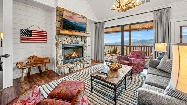 A cozy living room with a stone fireplace, a large window with a view, and a chandelier. - Haven| DogFriendly | BEST View | Hot Tub | Luxury (Gatlinburg)