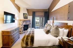 Une chambre avec une cheminée en pierre, un grand lit avec de nombreux oreillers, une commode et un téléviseur fixé au mur.