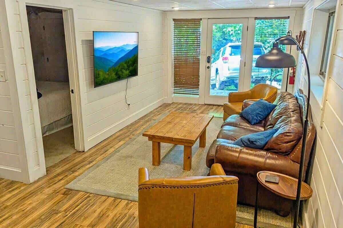 A living room with a wooden floor, a brown leather sofa, a wooden coffee table, and a television mounted on the wall.