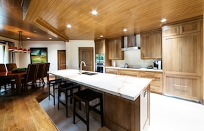 A modern kitchen with wooden cabinets, a marble island, and a dining area with a table and chairs.