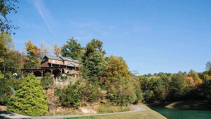 A lodge with a covered deck, surrounded by trees and a lake.