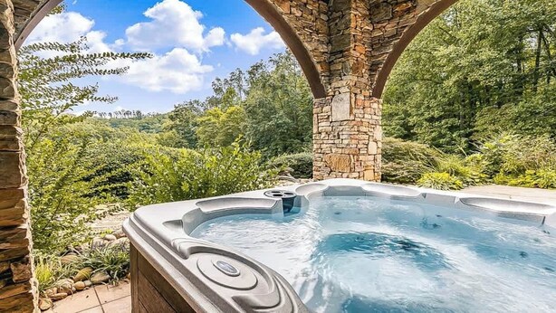 A hot tub under a stone archway surrounded by lush greenery.