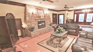 A living room with a stone fireplace, leather furniture, and a ceiling fan.