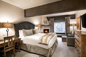 A bedroom with a large bed, a wooden desk, a dresser, and a fireplace.