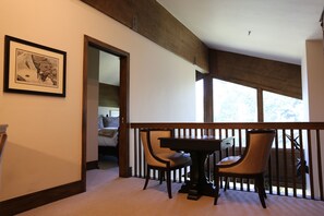 Ein Essbereich mit Tisch und Stühlen, einem gerahmten Bild an der Wand und Blick ins Freie durch große Fenster.