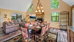 A dining area with a high ceiling, a fireplace, and large windows.