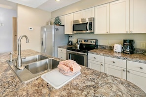 A kitchen with stainless steel appliances, a granite countertop, and white cabinetry.
