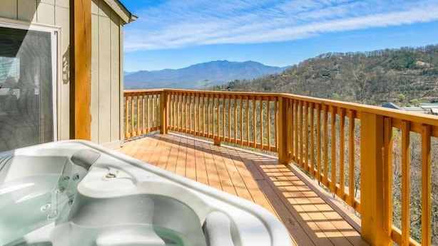 Eine Holzterrasse mit Whirlpool, einer Holzbrüstung und Blick auf Berge.