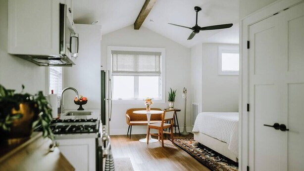 A compact kitchen with a stove, sink, and a dining area with a table and chairs. There is a window with a view of the outside, and a ceiling fan above.