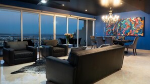 A modern living room with a large sofa, armchairs, and a dining table. There is a large window with a view of the cityscape. - Greatest view in the world! (Cabo San Lucas)
