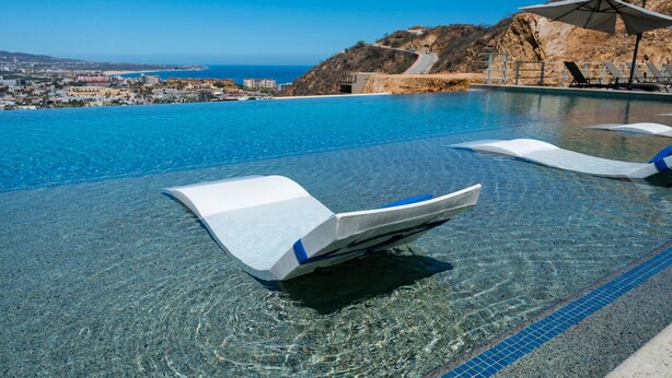 An infinity pool with clear blue water, lounge chairs, and a view of the coastline. - Greatest view in the world! (Cabo San Lucas)